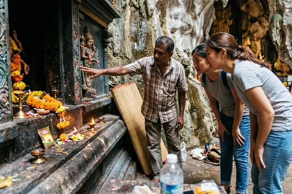 A guide pointing out carved detail on a shrine inside Batu Caves