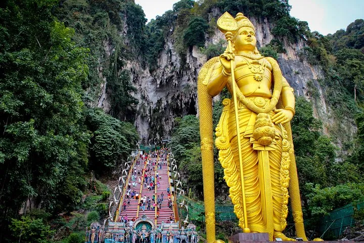 The golden Lord Murugan statue standing beside the staircase to Temple Cave at Batu Caves